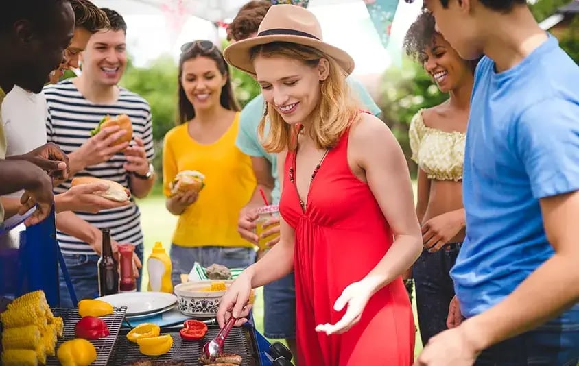 Friends grilling and preparing food together at an outdoor barbecue with burgers and vegetables