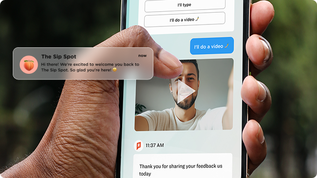 A hand holding a smartphone showing a chat-based Rival survey interface. The screen displays response options — 'I'll type' and 'I'll do a video' — with the video option selected in blue. A participant video thumbnail is visible in the chat. A push notification from 'The Sip Spot' appears in the upper left with a welcome-back message. A timestamped thank-you message is visible at the bottom of the chat